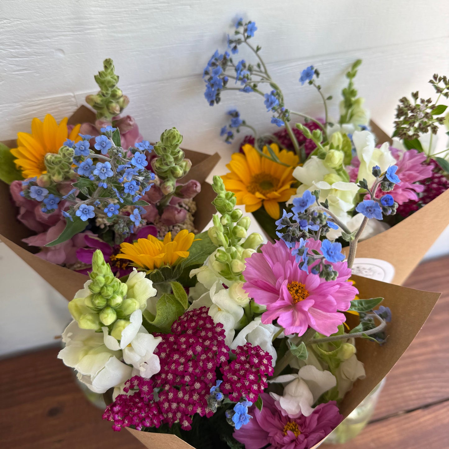 Bouquet of colorful flowers in brown paper packaging on a wooden surface.